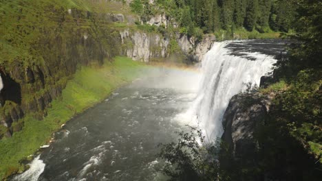 Spectacular-panoramic-scene-of-famous-upper-Mesa-falls-waterfall-cascading-down-side-of-mountain-steep-high-cliff-with-green-mossy-tree-lined-mountainside-in-background,-Idaho,-static-profile