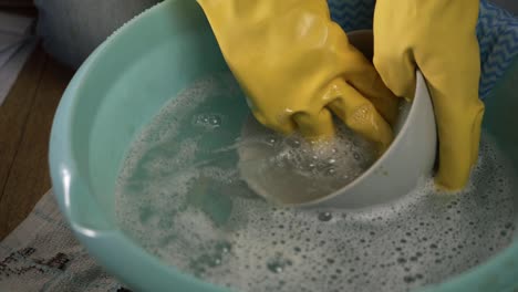 Hands-wearing-rubber-gloves-washing-dishes-medium-shot