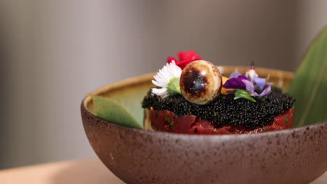 Salmon-Sushi-Roll-Topped-With-Black-Roe-And-Floral-Garnishes---close-up,-tracking-shot