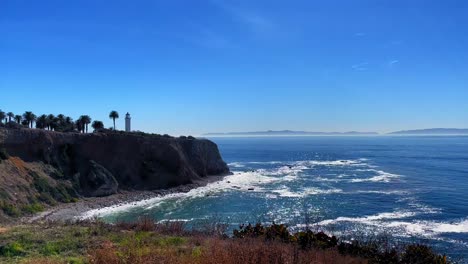 Standbildvideo-Von-Wellen,-Die-Auf-Den-Strand-Der-Klippen-Von-Rancho-Palos-Verdes-Schlagen,-Mit-Einem-Leuchtturm-Und-Der-Insel-Catalina-Im-Hintergrund