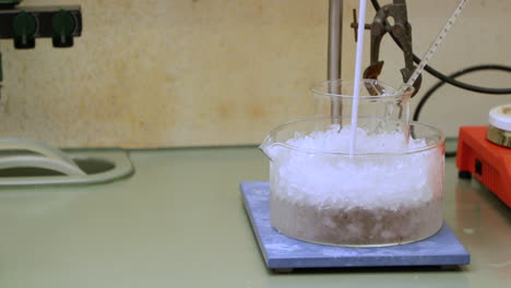 Chemical-Solution-In-A-Beaker-With-Thermometer,-Cooling-With-Ice-For-An-Experiment---close-up,-slow-motion
