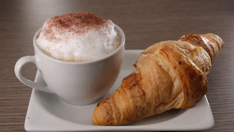 Pouring-cocoa-on-cappuccino-milk-coffee-and-brioche-croissant-breakfast