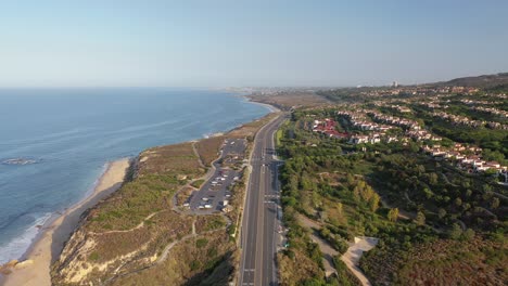 An-aerial-drone-shot-gliding-down-the-Orange-County-coastline-revealing-luxury-homes-with-a-view-of-crashing-ocean-waves-on-a-stunningly-sunny-day