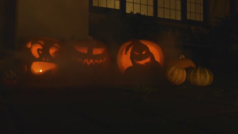 3-carved-lit-pumpkins-outside-the-front-of-a-house-Halloween-with-smoke-slow-motion