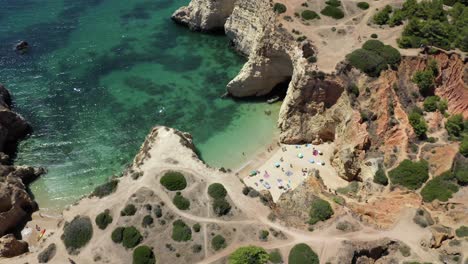 Incredible-tilt-up-reveal-of-local-Portuguese-families-on-a-private-secret-beach-surrounded-by-clear-green-ocean-water