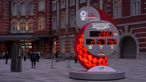 Tokyo-Olympic-Games-countdown-clock-in-front-of-Tokyo-Station-with-masked-commuters-passing-through-frame-during-Corona-Crisis-2020