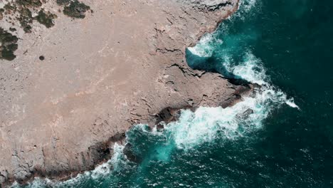 Top-View-Of-A-Blue-Waves-Breaking-And-Crashing-Against-The-Rocks-And-Cliffs-At-Cala-Figuera,-Santanyi,-Mallorca-In-The-Balearic-Islands-Of-Spain