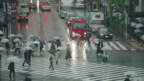 Fahrzeuge-Halten-An-Der-Shibuya-Kreuzung-An,-Während-Die-Menschen-An-Einem-Regnerischen-Tag-In-Tokio,-Japan,-Die-Kreuzung-überqueren