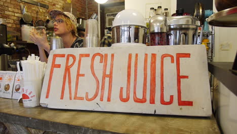 Hipster-Woman-Working-at-Fresh-Juice-Bar-Writes-Down-Order-at-the-Counter