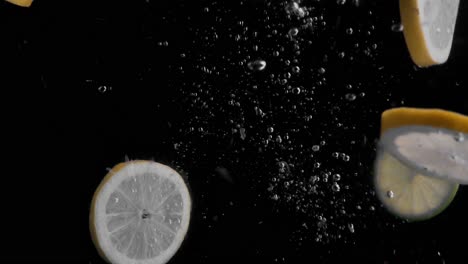 Zitronen--Und-Limettenscheiben-Fallen-In-Wasser,-Superzeitlupe,-Schwarzer-Hintergrund,-Viele-Luftblasen,-4k240fps