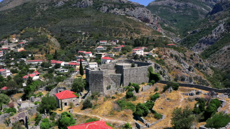Rotierende-4K-Luftaufnahme-Der-Festung-Stari-Bar-In-Montenegro-Mit-Einer-Bergschlucht-Im-Hintergrund-Und-Einer-Kleinen-Stadt-An-Ihrem-Fuß