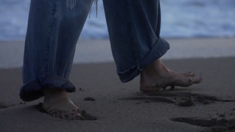 Girl-walking-barefoot-in-long-ripped-jeans-along-the-shore-of-the-beach-during-sunset