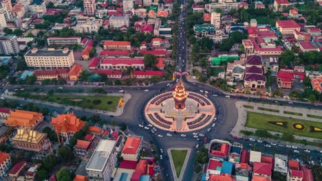 Bei-Sonnenuntergang-Beleuchtetes-Unabhängigkeitsdenkmal-Mit-Fahrenden-Fahrzeugen-An-Der-Kreuzung-Von-Norodom-Und-Sihanouk-Boulevard-In-Phnom-Penh,-Kambodscha