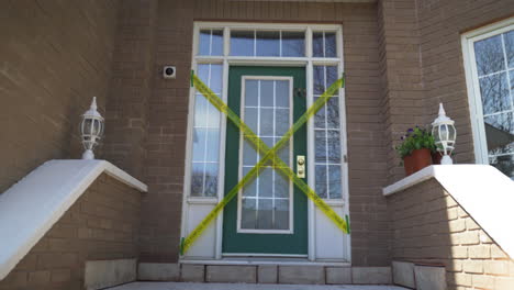 Crime-scene-do-not-cross-yellow-tape-across-front-door-of-brick-home-entranceway