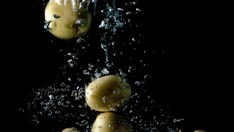 Potatoes-dropped-into-water-on-black-background,-slow-motion-close-up
