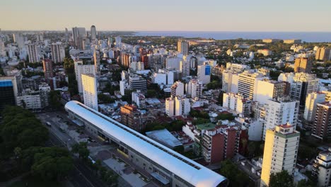 Orbital-flying-over-Belgrano-neighborhood-train-station-with-Rio-de-la-Plata-river-in-background,-Buenos-Aires,-Argentina