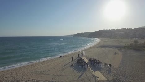 Luxury-romantic-tropical-sandy-beach-wedding-service-ceremony-rising-aerial-above-sunset-coastline