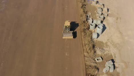 Aerial-following-shot-of-a-Bulldozer-roller-compacting-dirt-in-a-field-next-to-drain-pipes