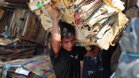 Man-Carrying-Bundle-Of-Cartons-For-Recycling-In-Indonesia---medium-shot,-slow-motion