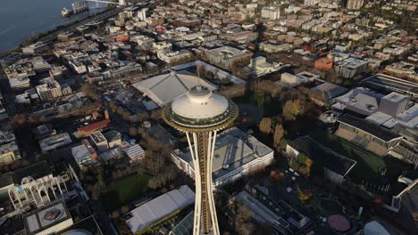 The-Seattle-Space-Needle-stands-proudly-above-dense-urban-sprawl,-sunrise,-aerial-orbit