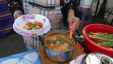 Thai-woman-ladling-Tom-Yum-soup-into-bowl-to-be-served-as-healthy-meal