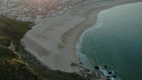Rayo-De-Sol-Sobre-El-Paisaje-Urbano-En-La-Playa-De-Arena-De-Praia-Do-Norte,-Nazare-Portugal