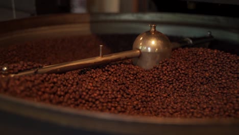 Traditional-golden-open-coffee-roasting-machine-roasting-fresh-coffee-beens-turning-them-around-with-its-shovel,-beans-falling-slowly-in-slowmotion-roaster