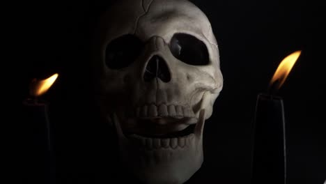 Human-skull-closing-mouth-between-two-candles-on-dark-background