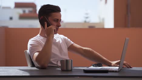 Confident-young-businessman-talking-on-mobile-phone-while-working-on-the-laptop