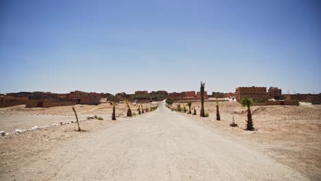 Dry-road-leading-to-small-village-with-buildings-in-sahara-desert,-static-shot