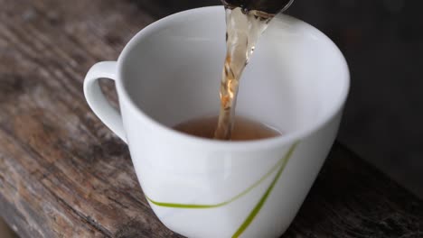 Slow-motion-shot-of-pouring-a-cup-of-tea-in-a-white-mug-on-a-wooden-table