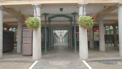 Lone-person-walks-across-rows-of-closed-shops-in-empty-lockdown-Covent-Garden-Market-Piazza-with-beautiful-symmetrical-columns,-during-2020's-COVID-19-pandemic