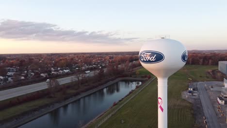 Water-Tower-Of-Ford-Woodhaven-Stamping-Plant-In-Wyandotte,-Michigan-Overlooking-Busy-Highway-On-A-Sunset---aerial-arc-shot