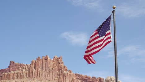 Slow-motion-shot-of-USA-flag-blowing-in-the-wind-in-front-of-huge-rocks-in-Capitol-Reef-National-Park-in-Utah,-USA