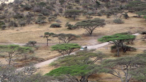 Epic-Wide,-High-Angle-View-of-a-Safari-Jeep-Driving-Down-a-Dirt-Road-in-Serengeti-National-Park-in-Tanzania,-Slow-Motion