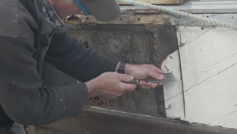 Carpenter-scrapes-off-paint-to-locate-screws-on-wooden-boat-Seaplane-Tender-restoration