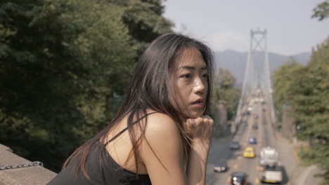 Medium-Closeup-of-asian-woman-in-black-looking-forward,-Lions-gate-bridge-in-background,-Slowmo