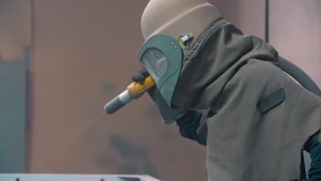 Arbeiter,-Der-In-Der-Werkstatt-Eine-Maske-Mit-Sandstrahl-Auf-Der-Metalloberfläche-Trägt