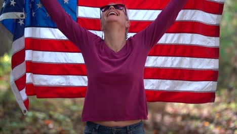 Mujer-Rubia-Levantando-Una-Bandera-Americana-Detrás-De-Ella-Con-Expresión-Sonriente