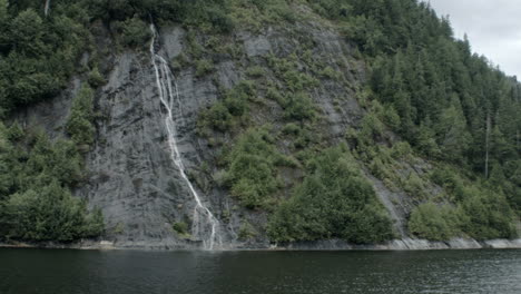 Small-waterfalls-run-down-a-mountain-into-the-ocean-water-of-an-Alaskan-fjord