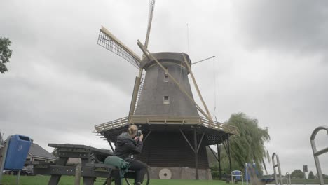 Tourism-in-the-Netherlands---a-Young-Woman-Sitting-Down-Takes-a-Picture-of-an-Old-Windmill