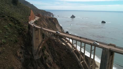 Aerial-Drone-Stock-Video-of-Cars-passing-on-Bixby-Bridge-Highway-with-water-and-shore-below-in-Big-Sur-Monterrey-California