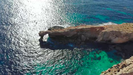 Drone-shot-over-rocks-in-nature-and-towards-a-natural-stone-window-on-the-Mediterranean-sea-of-Malta