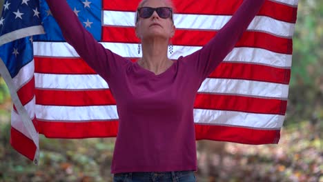 Mujer-Rubia-Levantando-Una-Bandera-Americana-Detrás-De-Ella-Con-Expresión-Seria