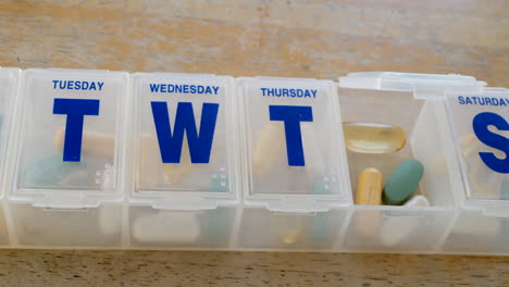 Close-up-on-a-medical-prescription-pill-box-organizer-full-of-vitamins-and-health-supplements-with-a-glass-of-water
