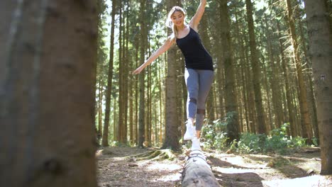 Young-woman-in-athletic-attire-walks-playfully-across-a-fallen-tree-using-her-hands-for-balance-and-kicks-her-leg-before-hopping-down
