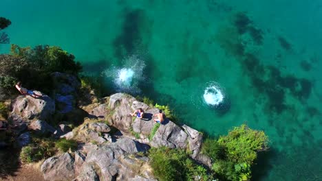 Swimmers-jump-into-beautiful-clear-water-off-a-cliff-from-an-aerial-view