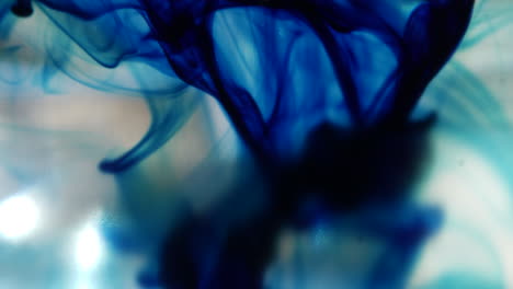 Macro-shot-of-blue-ink-drops-as-it-spreads-out-slowly-underwater-and-creates-smokey-abstract-shapes-in-the-background