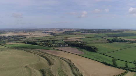 High-up-aerial-tracking-forward-over-Maiden-Castle-looking-south,-Sea-is-just-visible-on-the-horizon,-with-a-mixture-of-livestock-and-arable-fields-in-the-mid-ground