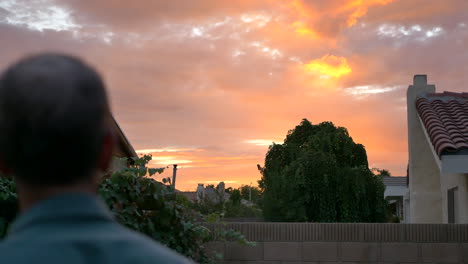 A-middle-aged-man-stares-in-awe-at-a-colorful-orange-sunset-from-his-suburban-home-backyard-in-Los-Angeles,-California